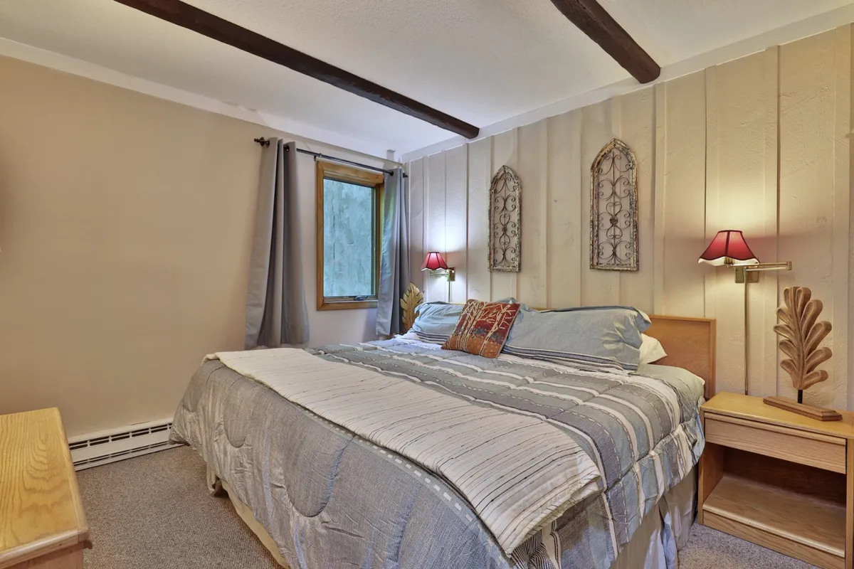 A spacious bedroom featuring a large bed with crisp, inviting bedding, complemented by decorative wall art and warm table lamps on each side. Natural light flows through the room, creating a tranquil environment ideal for a restful night's sleep.