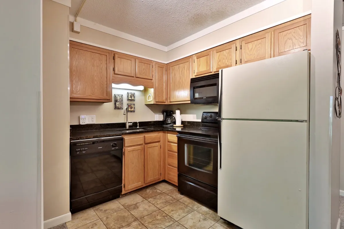 A functional kitchen space with sleek black appliances, warm wood cabinetry, and ceramic tile flooring. The kitchen is fully equipped, spacious, and ready for everything from quick breakfasts to group meal preparations.