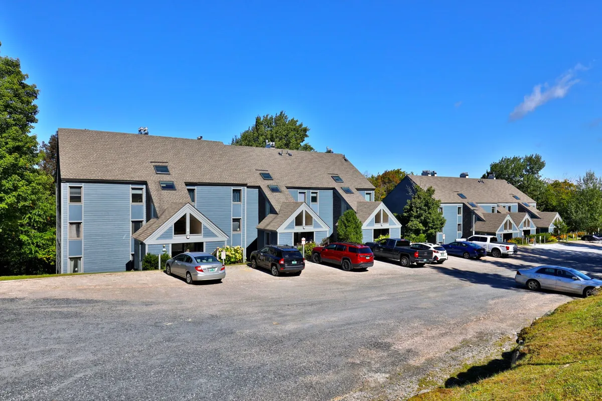 This exterior scene features residential buildings surrounded by green trees and parked cars, evoking a sense of a welcoming community. The open outdoor spaces hint at areas where families can gather, kids can play, and community events can take place.