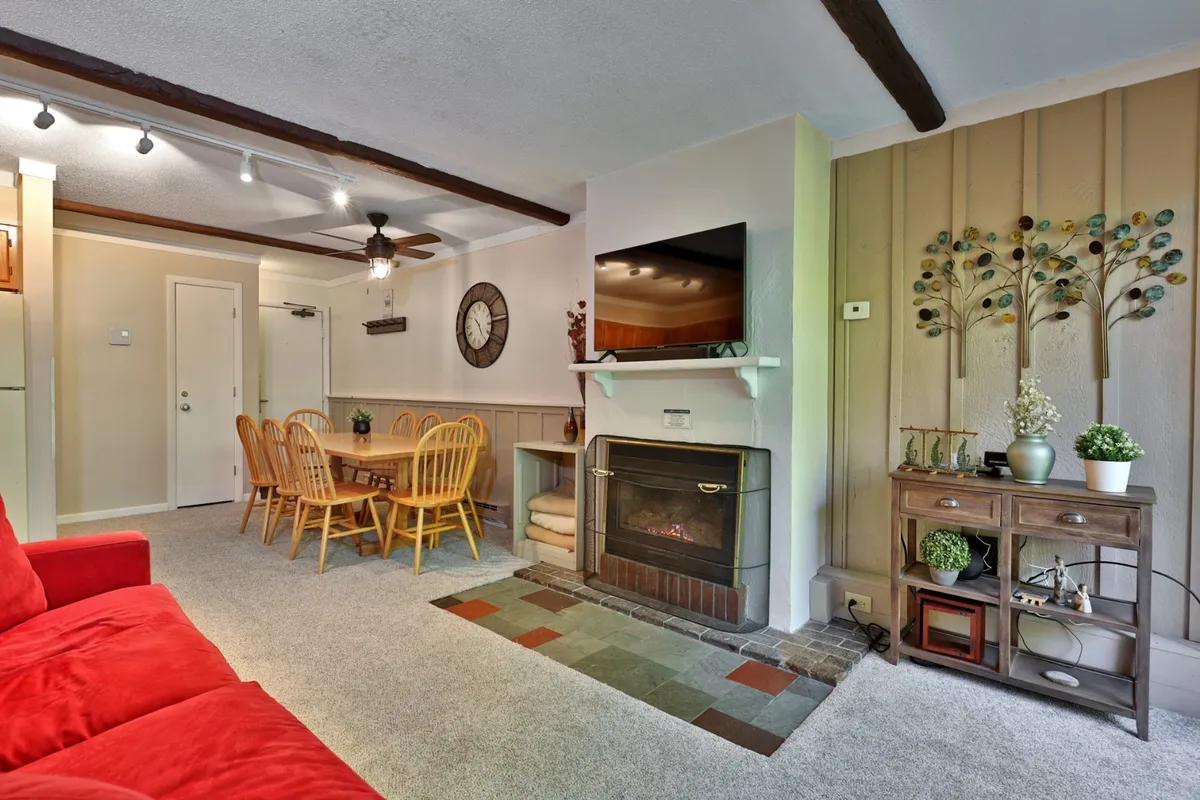 A warm, open-plan living room featuring a cozy red sofa, inviting fireplace, dining table set for gathering, a mounted TV, and tasteful wall art. The room exudes comfort, ideal for relaxing after a day on the slopes or socializing with family and friends.
