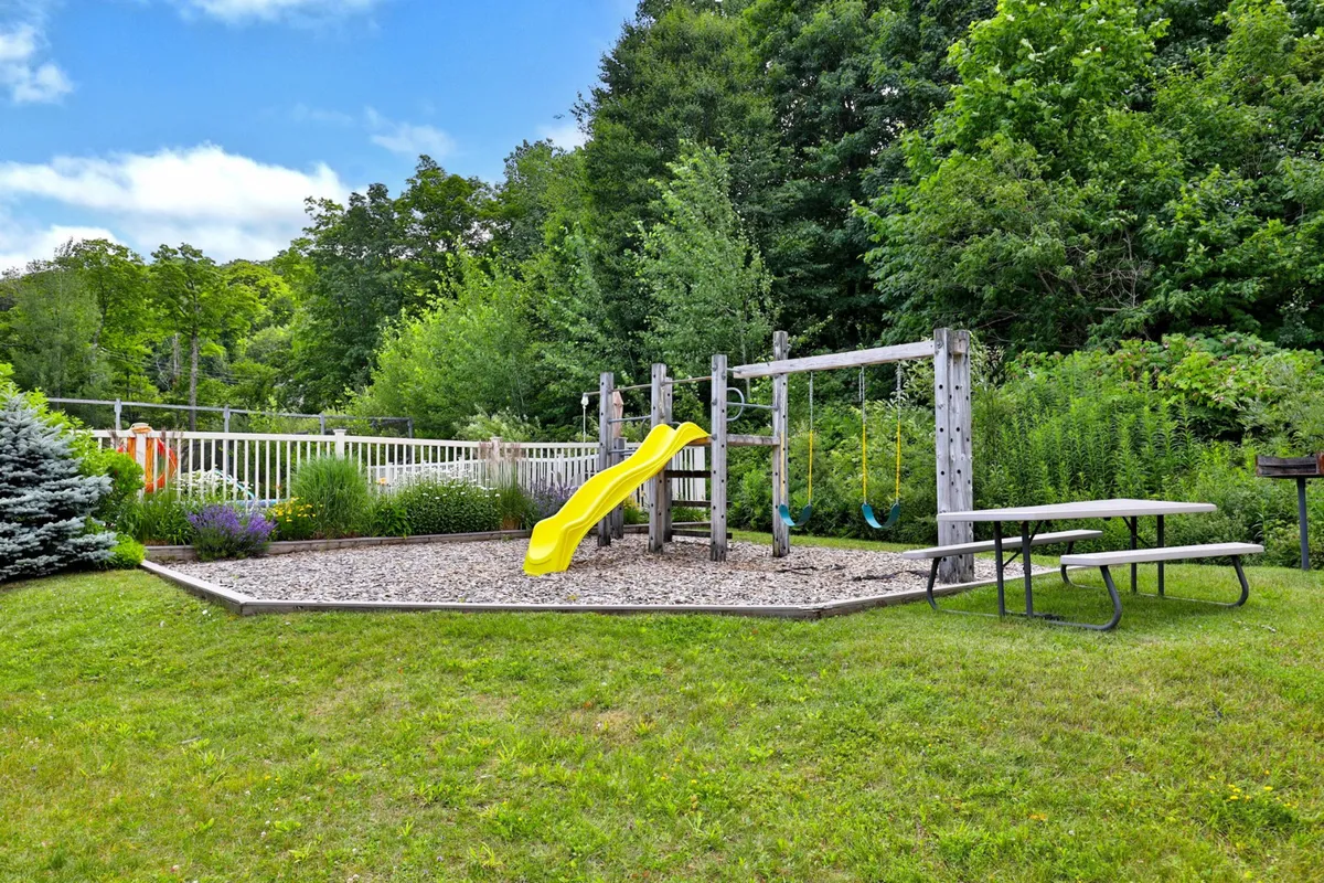 A cheerful playground with a slide, swing set, picnic table, and lush surroundings, capturing the joyful spirit of family gatherings and children's playtime outdoors.