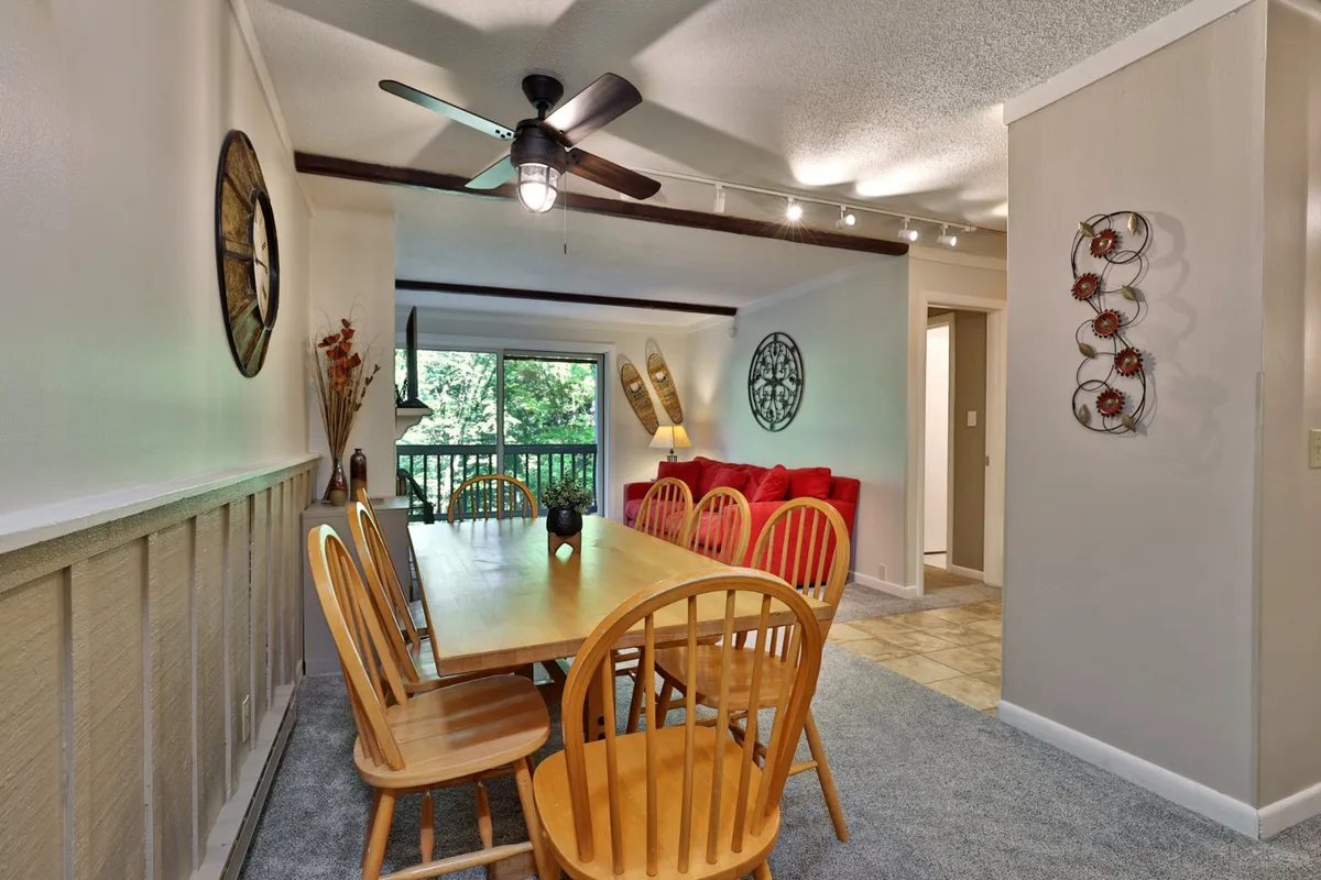A welcoming dining area with a wooden table, red couch, expansive window letting in mountain light, and decorative wall art. The space feels bright, comfortable, and ideal for shared meals or game nights.