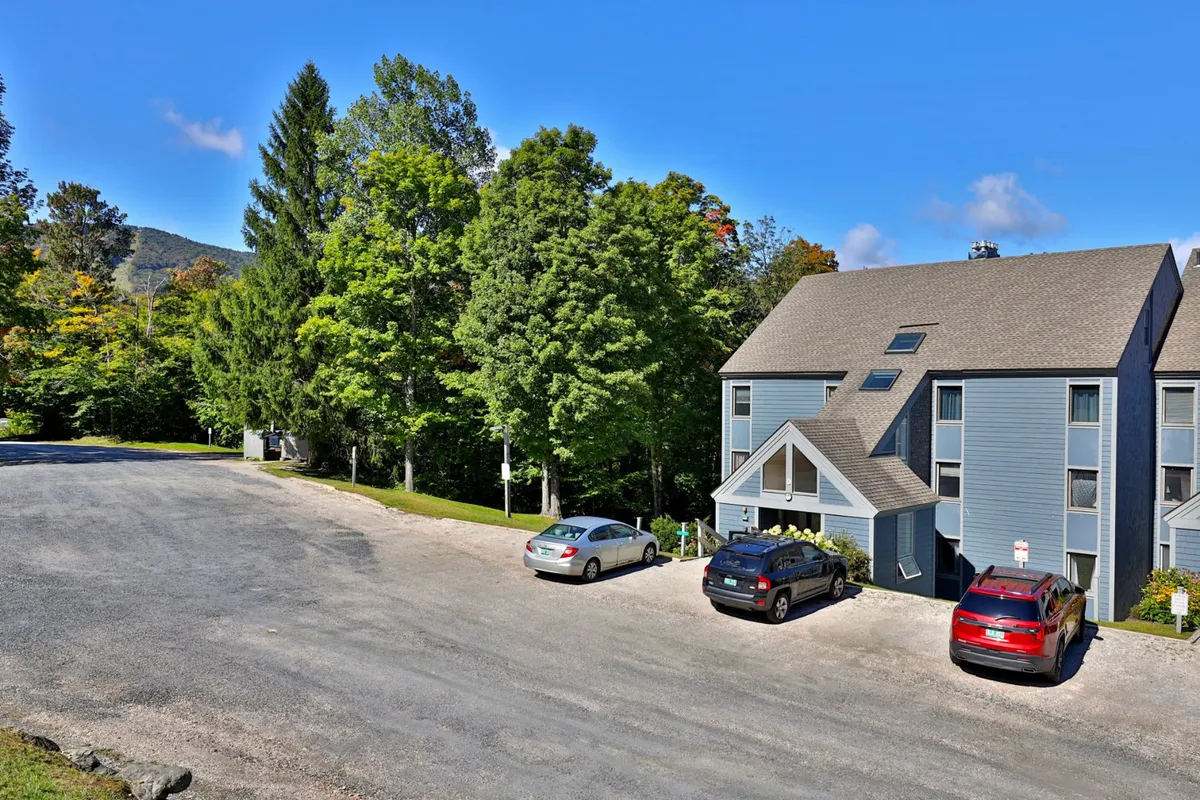 This exterior shot captures the building nestled among mature trees, with cars parked in the lot, suggesting easy access for guests returning from local hotspots. The environment feels peaceful yet connected to community life.