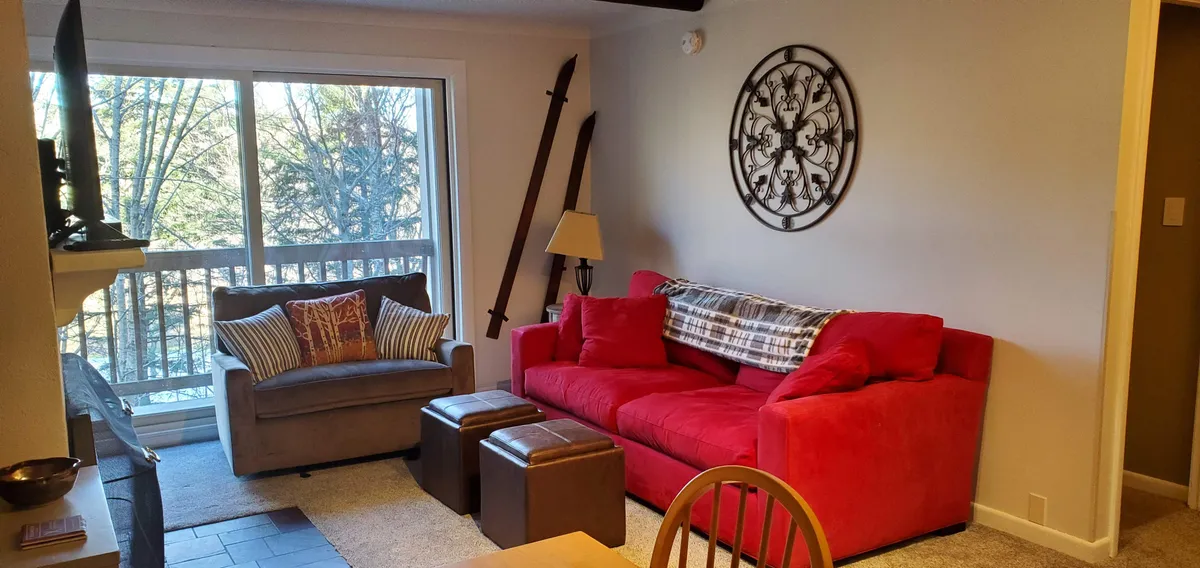 A cozy living space with a red sofa, decorative wall art, and a large window offering a glimpse of the natural world outside. The room feels warm and welcoming, ideal for relaxing after outdoor adventures.