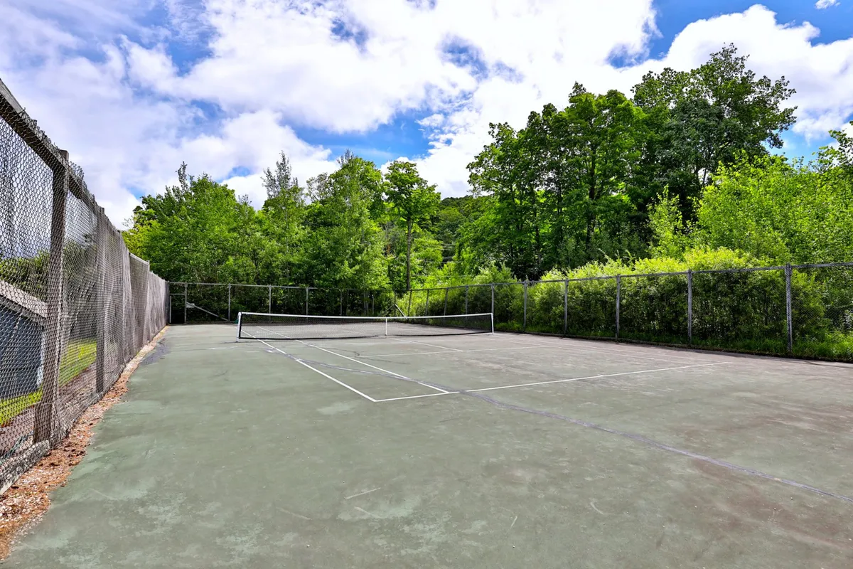 A vibrant tennis court bordered by greenery and a secure fence, inviting guests to enjoy energetic matches and outdoor recreation. The well-maintained space emphasizes active community living.